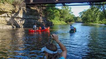 A river scene with a bridge, people in canoes, and a person taking a photo.