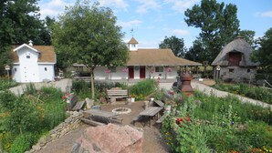 A rustic garden with stone structures, a wooden bench, and a fire pit. - Cupola Inn Bed & Breakfast (Nora Springs)