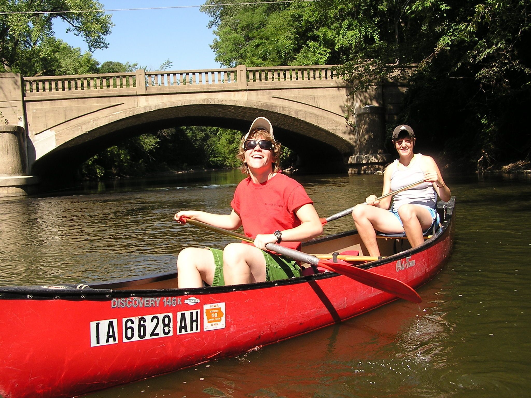 Dos personas en un canoa roja en un río, con un puente al fondo.