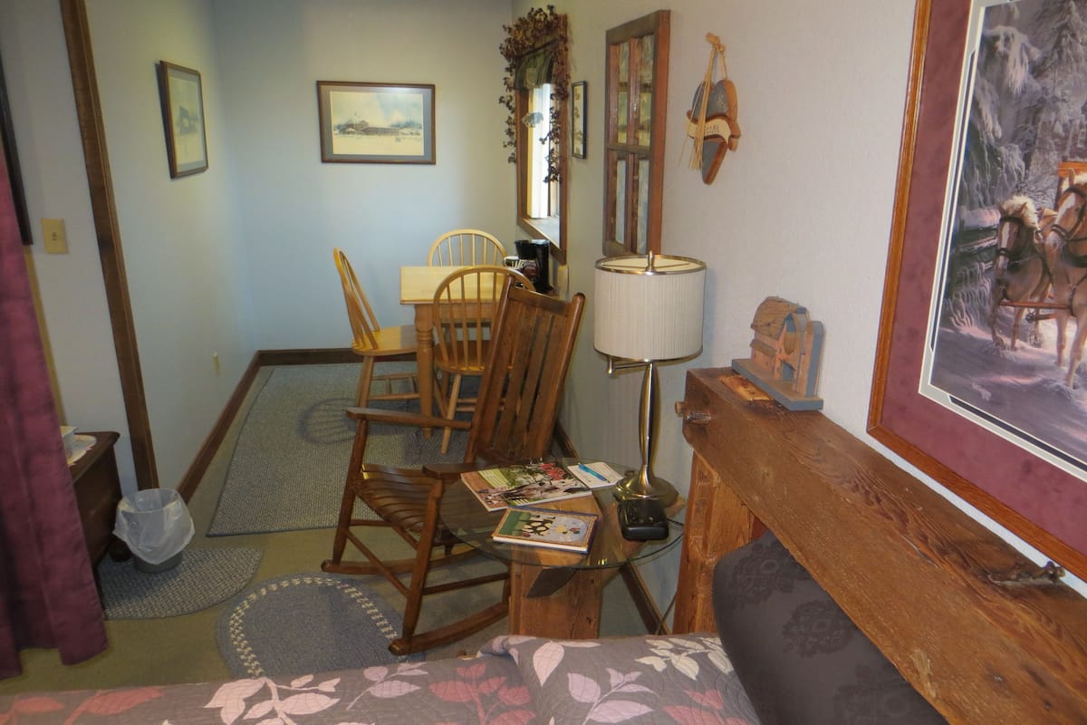 A cozy room with a wooden dining table, a rocking chair, a sofa, and a framed picture on the wall.