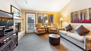 A living room with a fireplace, a television, two armchairs, a sofa, and a painting on the wall. - Evergreen Hill Condominiums (Fish Creek)
