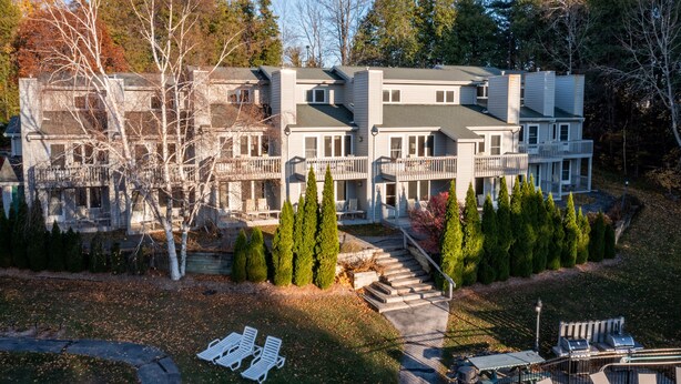 A multi-story building with a central staircase, surrounded by trees and a well-maintained lawn. - Evergreen Hill Condominiums (Fish Creek)