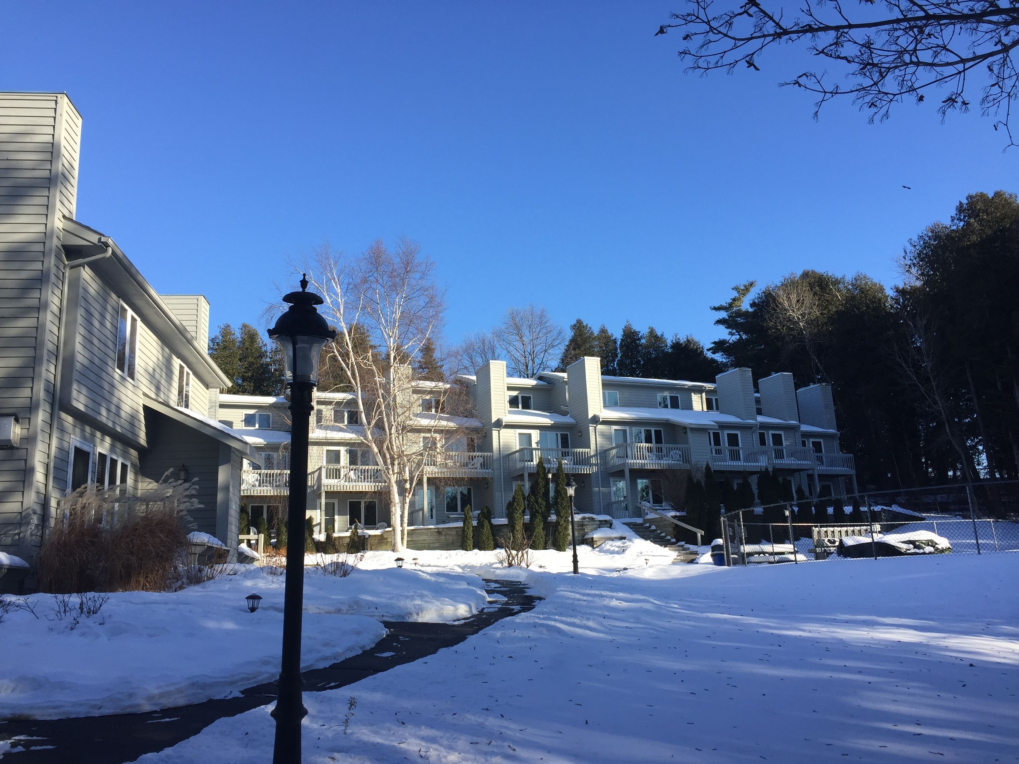 Ein Wohngebiet mit verschneiter Straße, Häusern mit Balkonen und wolkenlosem, blauem Himmel.