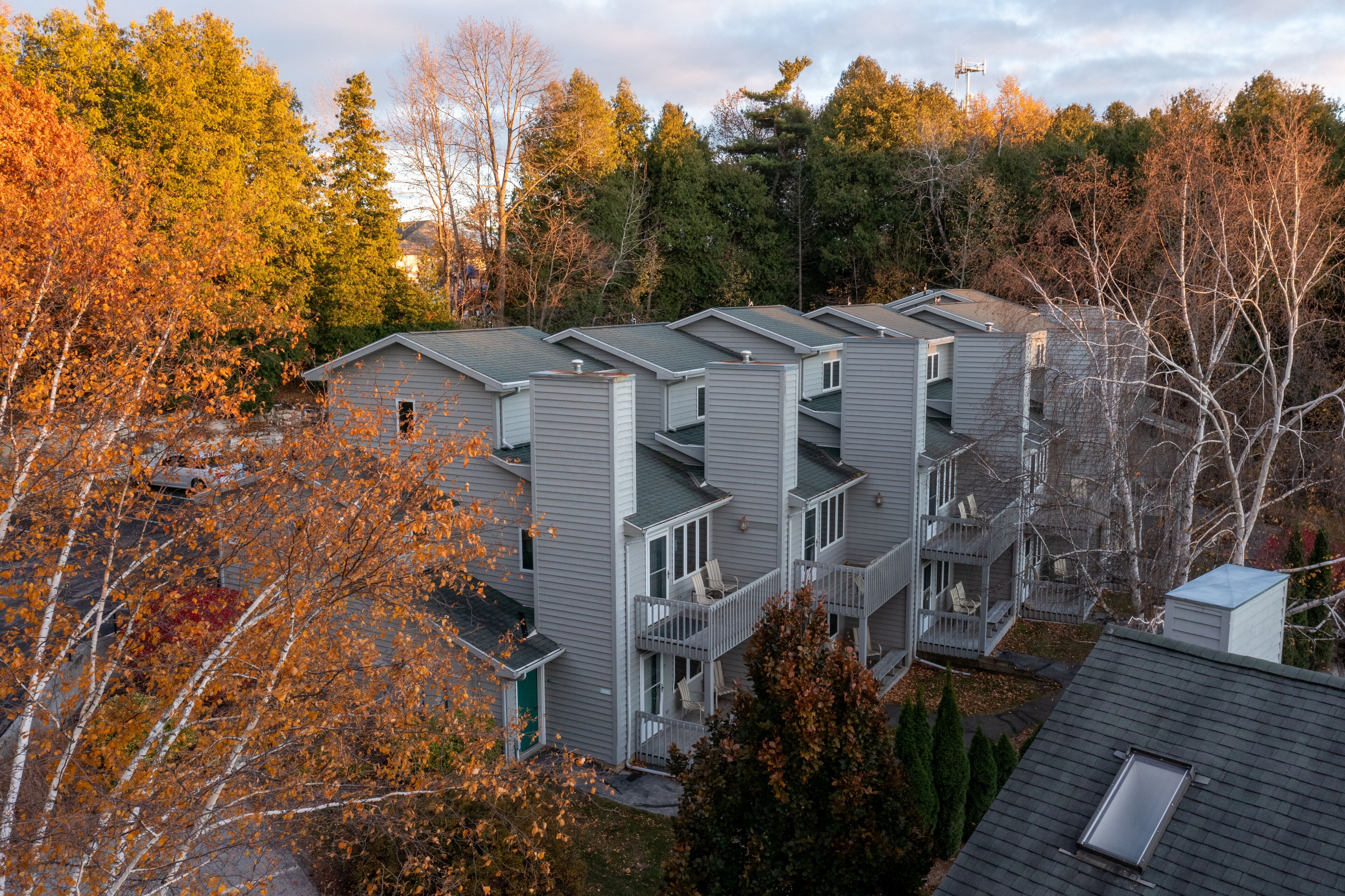 A row of modern, multi-story apartment buildings with balconies, surrounded by autumn foliage.