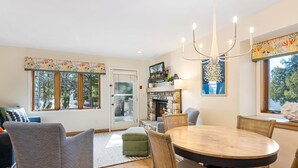 A dining area with a round table and chairs, a fireplace, and a view of trees through the windows. - Evergreen Hill Condominiums (Fish Creek)