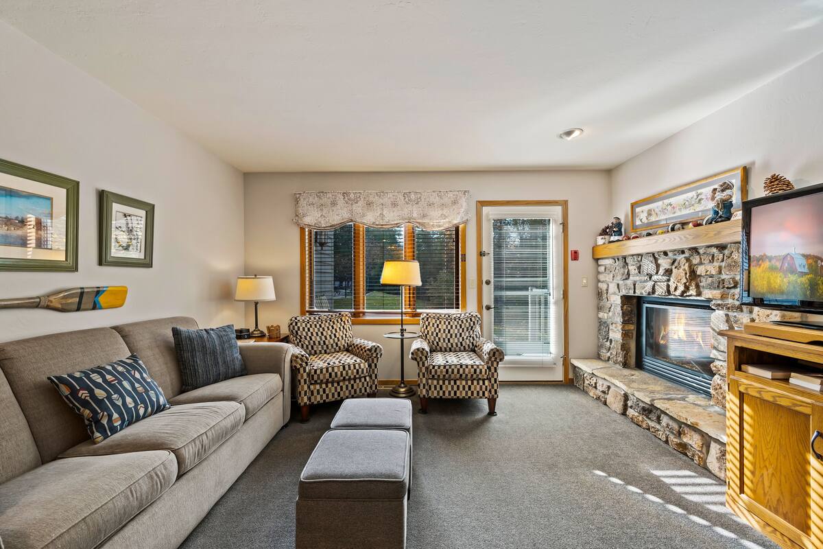 A cozy living room with a sofa, two armchairs, a coffee table, a fireplace, and a television.
