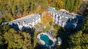 An aerial view of a residential area with multiple houses, a swimming pool, and surrounding trees. - Evergreen Hill Condominiums (Fish Creek)