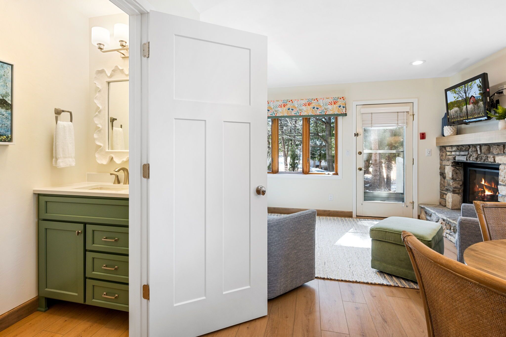 A well-lit room with a white door, a green cabinet, a fireplace, and a dining area with a table and chairs.