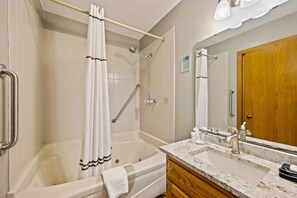 A bathroom with a bathtub, shower, vanity with a sink, and a wooden door. - Evergreen Hill Condominiums (Fish Creek)