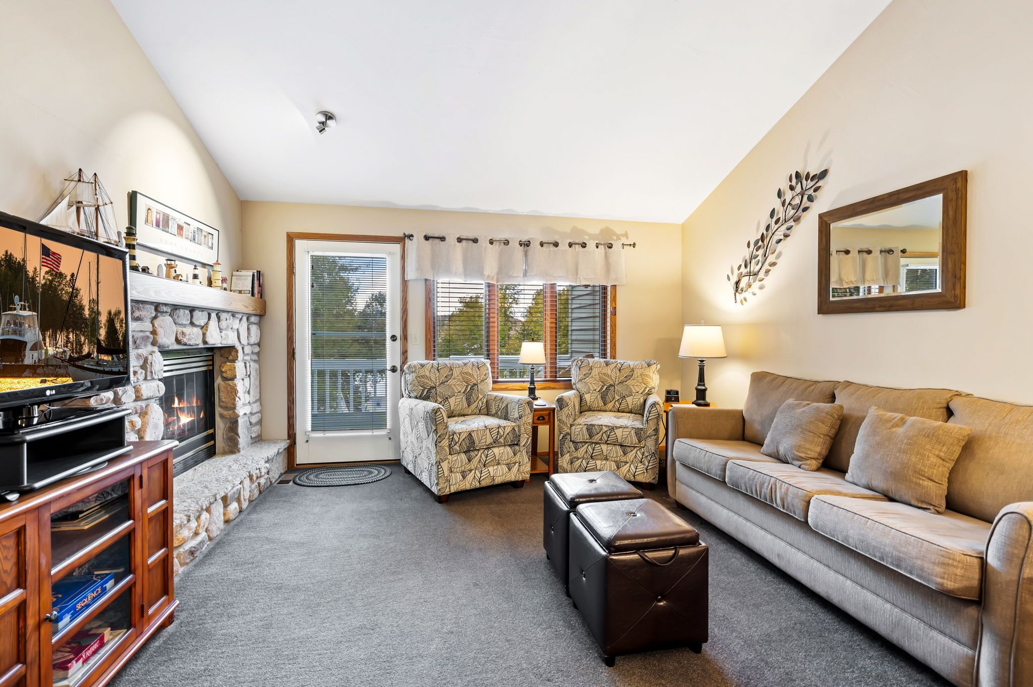 A living room with a stone fireplace, two armchairs, a sofa, a television, and a large mirror.