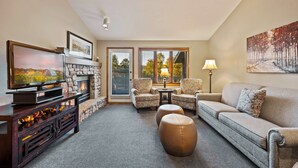 A living room with a fireplace, a television, two armchairs, a sofa, and a painting on the wall. - Evergreen Hill Condominiums (Fish Creek)