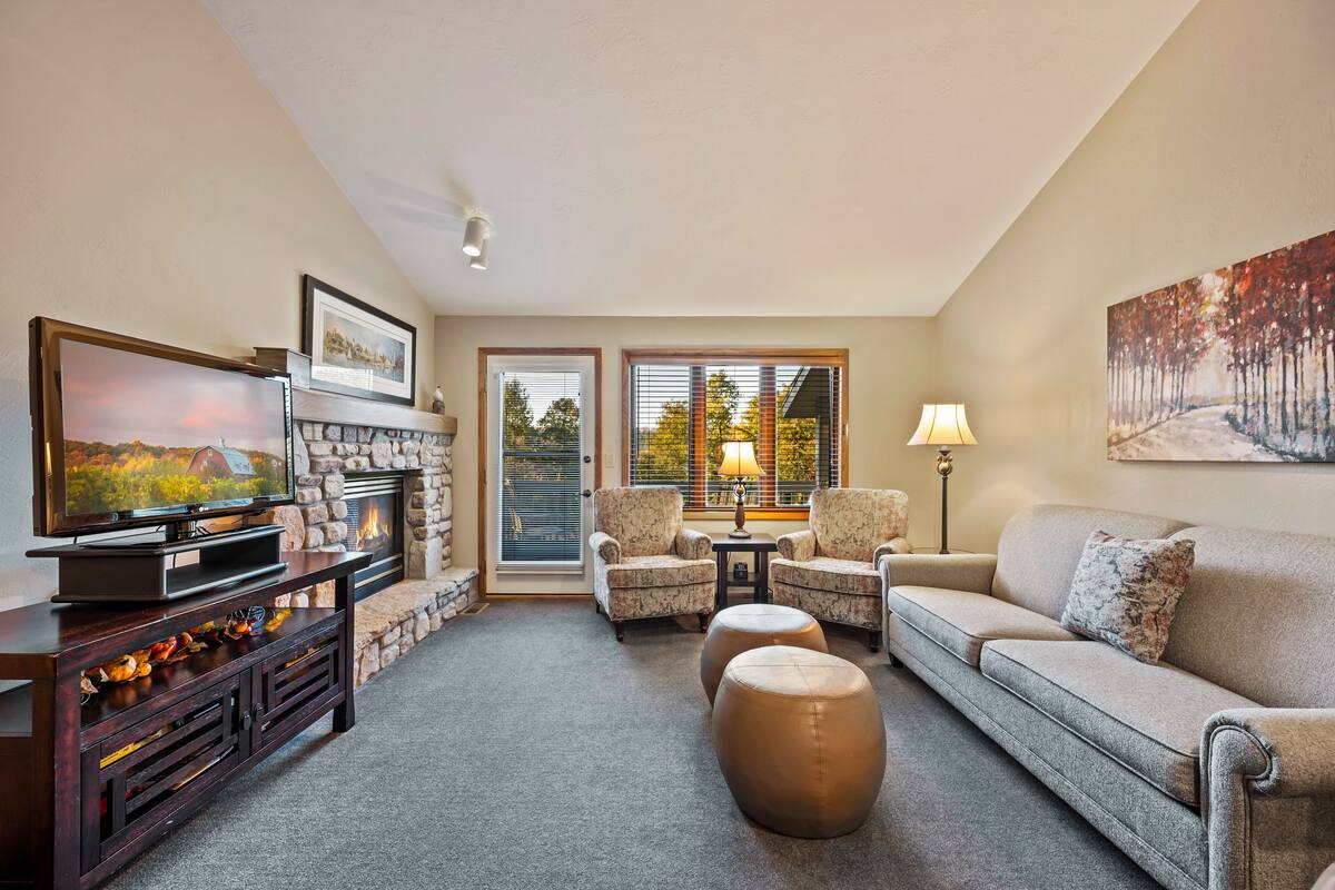 A living room with a fireplace, a television, two armchairs, a sofa, and a painting on the wall.