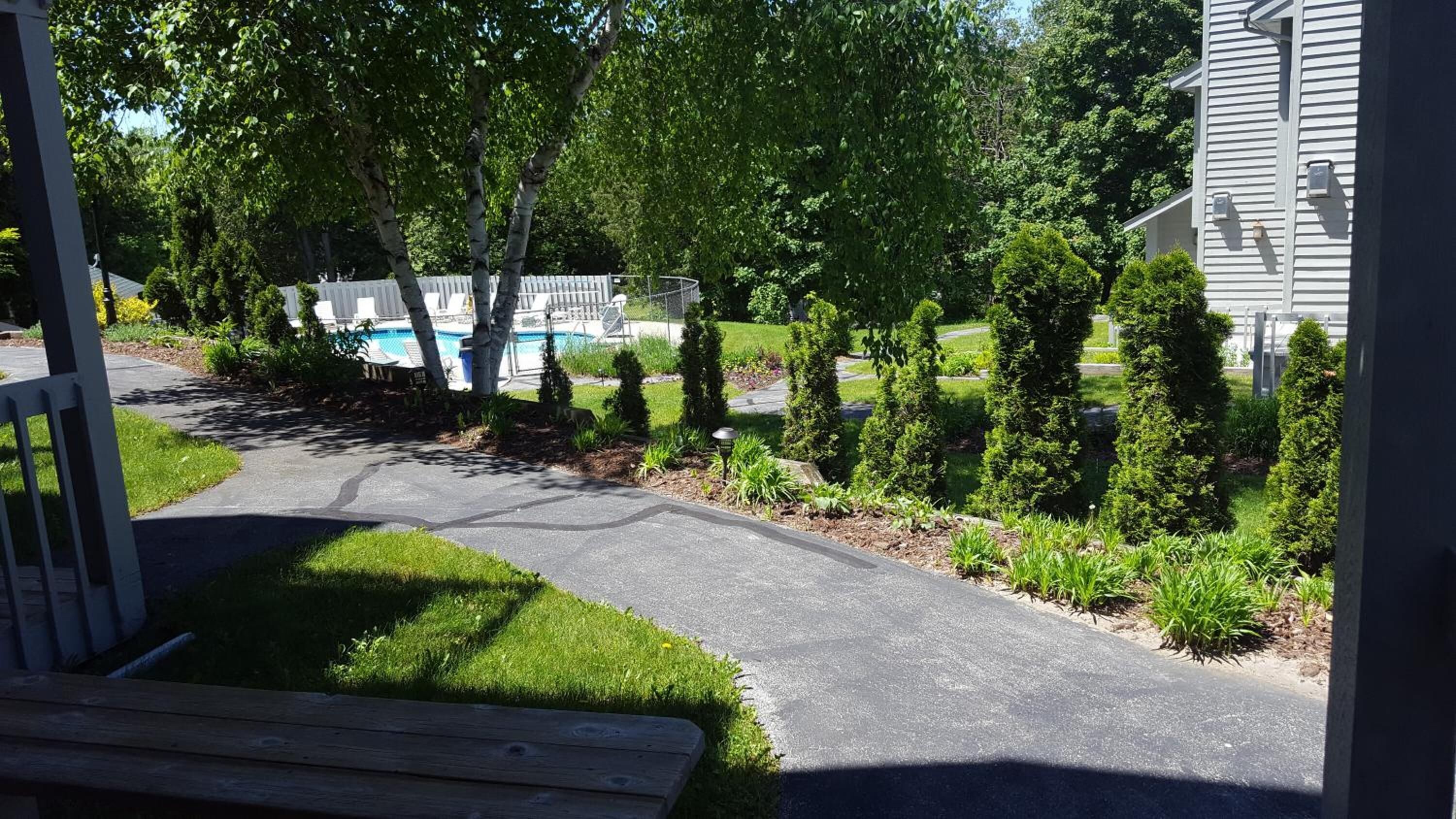 Un camino de entrada residencial con piscina, setos cuidadosamente podados y una terraza de madera.