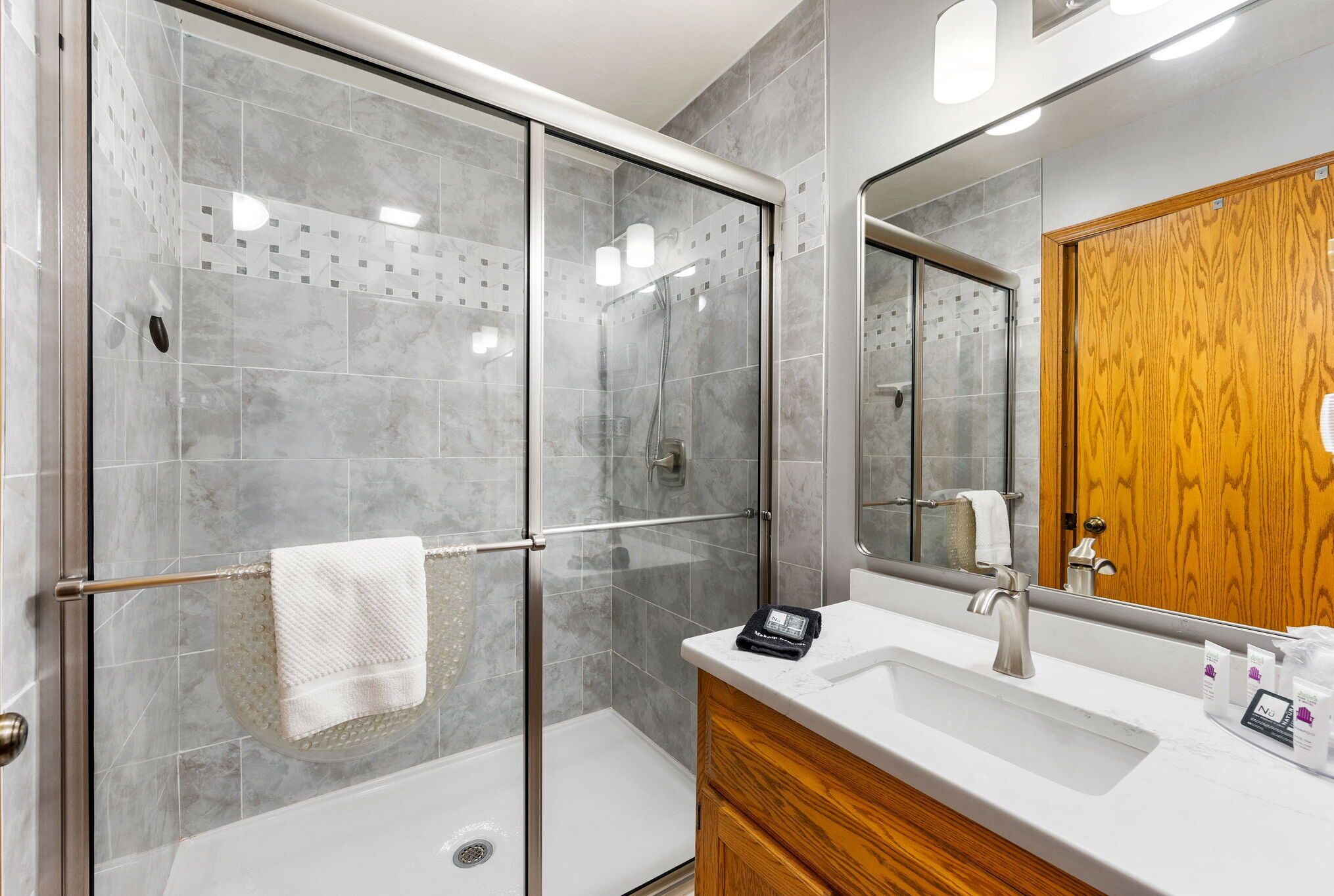 A modern bathroom with a glass-enclosed shower, a wooden vanity, and a large mirror.