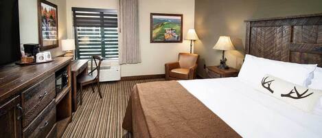 A hotel room with a bed, a desk with a chair, a lamp, and a painting on the wall.