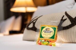 A package of Angler's Lodge gummy worms on a bed with a pillow featuring a fish design. - Angler's Lodge Hollister (Hollister)