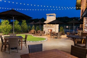 An outdoor patio area with tables and chairs, string lights, and a stone fireplace.