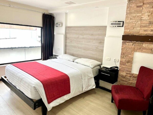 A modern hotel room with a bed, a red chair, a nightstand, and a view of the outside.