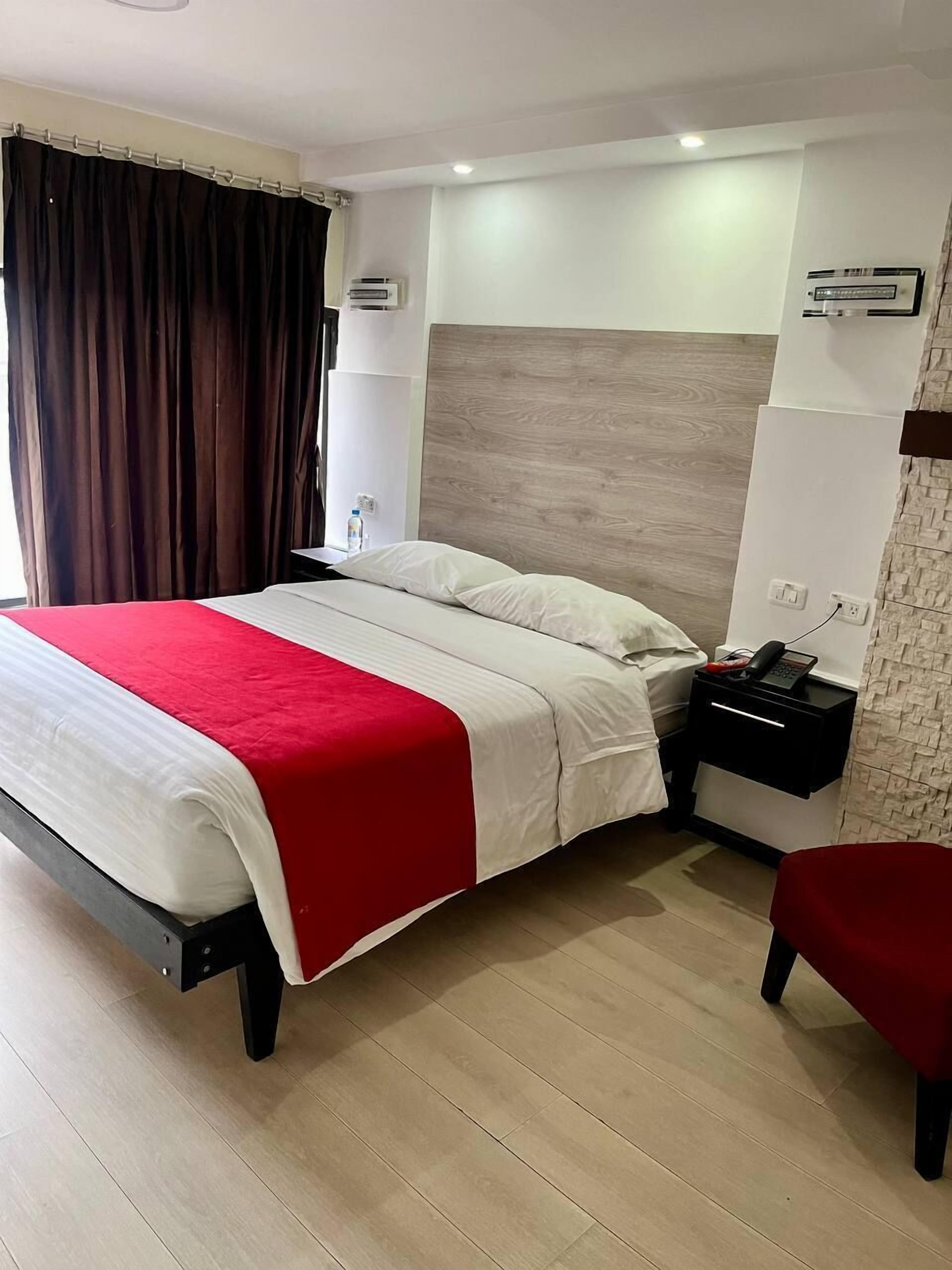 A hotel room with a bed, a nightstand, a phone, and a chair.