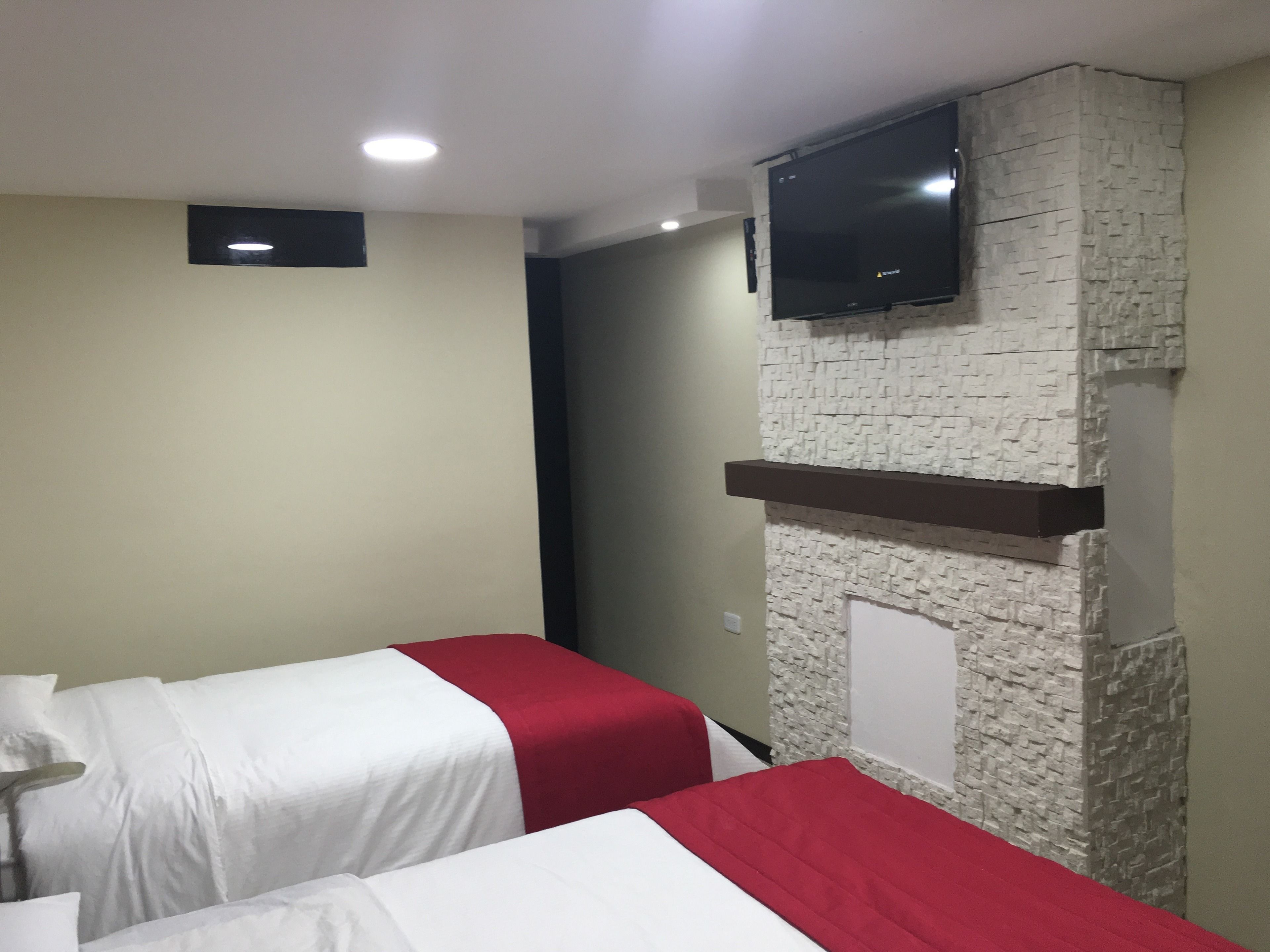 Una habitación de hotel con dos camas, un televisor de pantalla plana montado en una pared de piedra y un estante pequeño debajo.