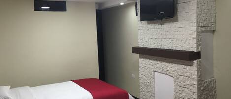 Una habitación de hotel con dos camas, un televisor de pantalla plana montado en una pared de piedra y un estante pequeño debajo.