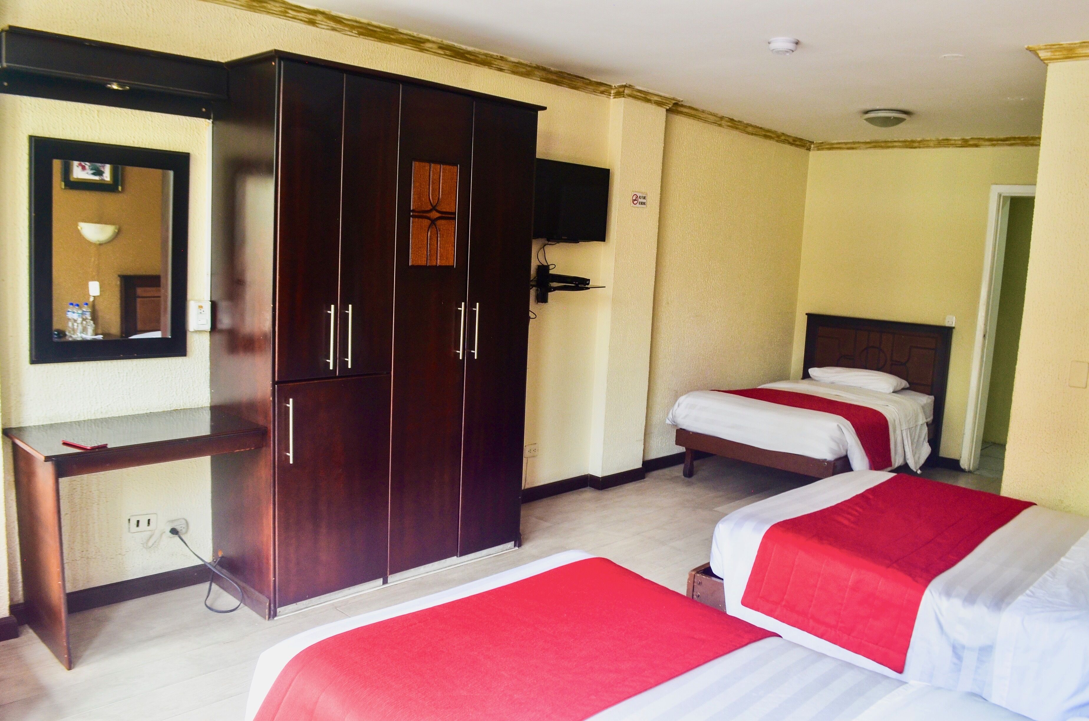 A hotel room with two beds, a wardrobe, a desk with a mirror, and a television on the wall.