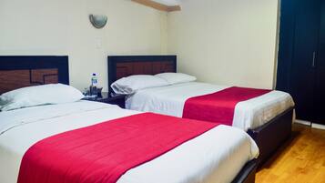 A hotel room with two beds, each with a red and white bedspread, a nightstand with a bottle, and a wooden floor.
