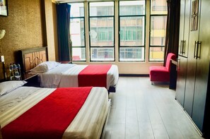 A hotel room with two beds, a wardrobe, and a window with a view of buildings.