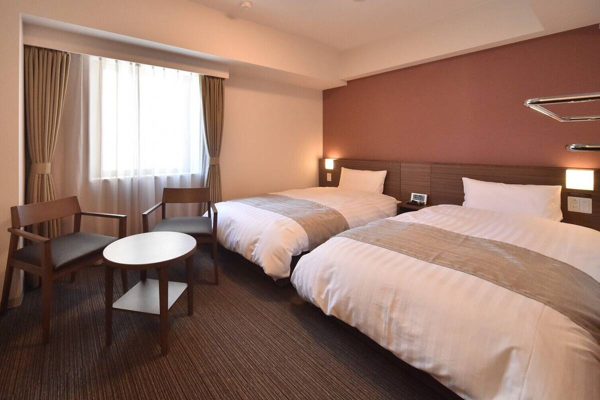 Habitación de hotel con dos camas, un escritorio y una silla.