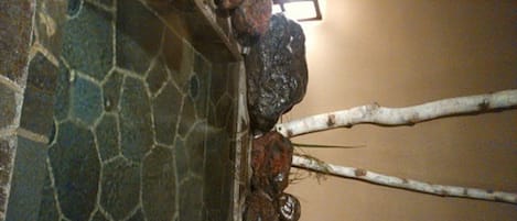 A stone wall with a small water feature and a wooden beam.