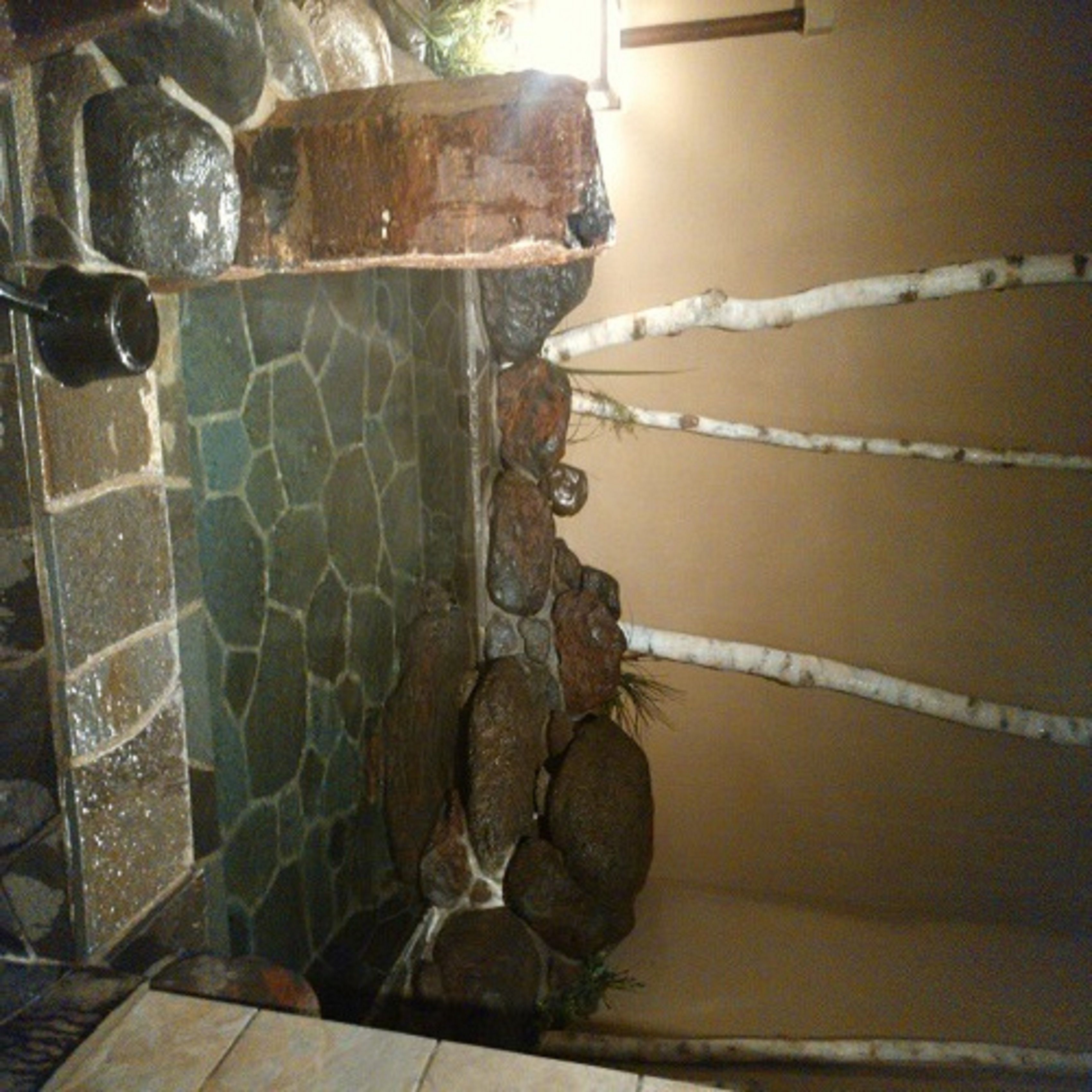 Una pared de piedra con una fuente de agua y un estante de madera.