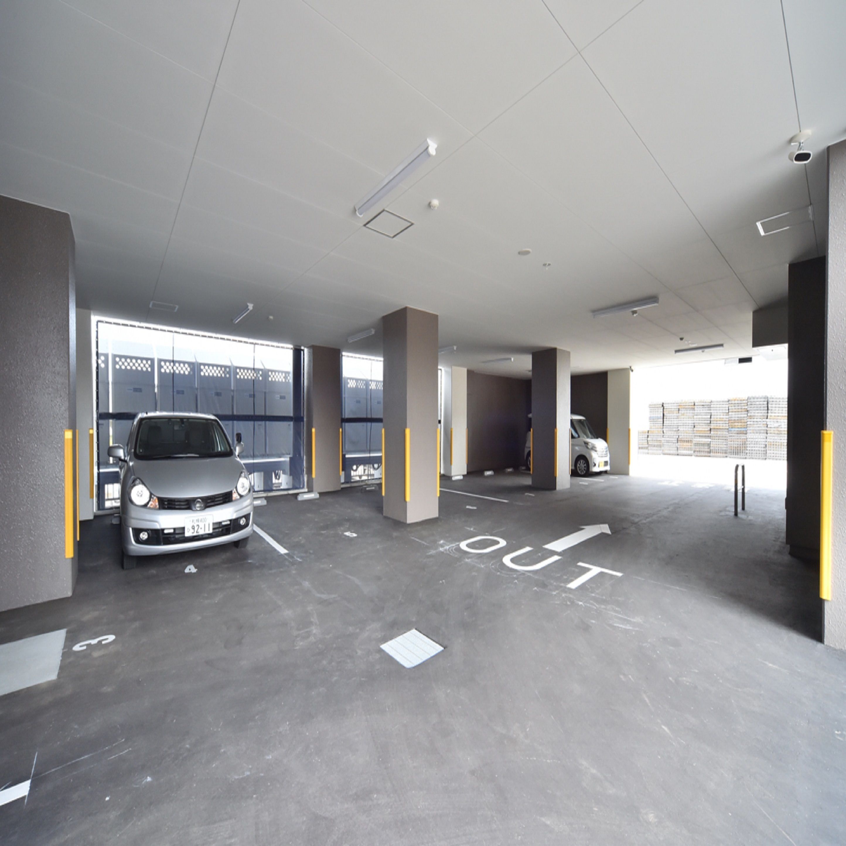 A parking garage with two cars parked, marked exit signs, and a view of a fenced area outside.