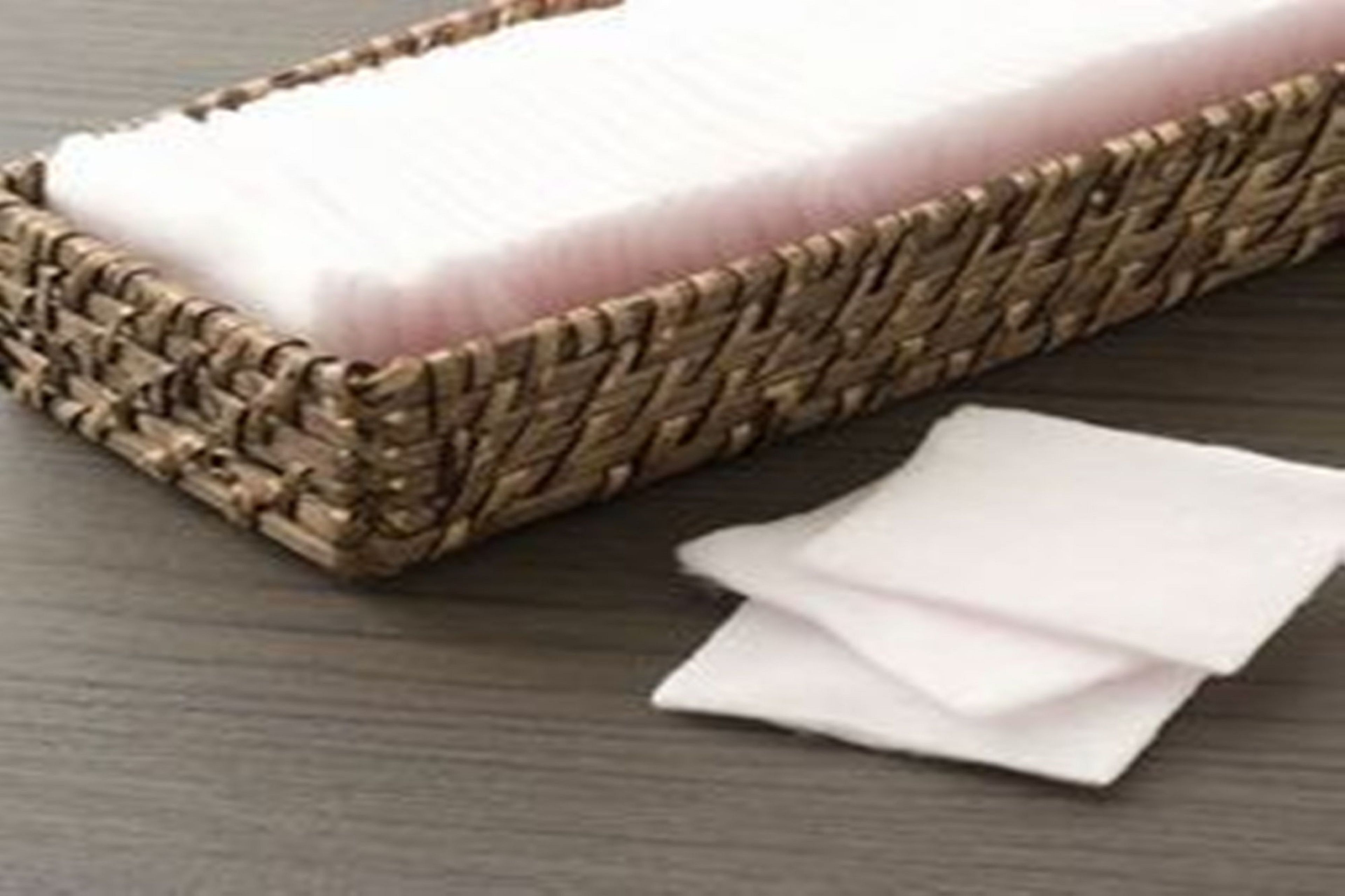A woven basket containing a white object, possibly a cleaning tool, and a few white cloths on a wooden surface.