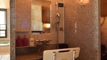 A bathroom with a shower, a sink, a mirror, and a wheelchair-accessible chair.