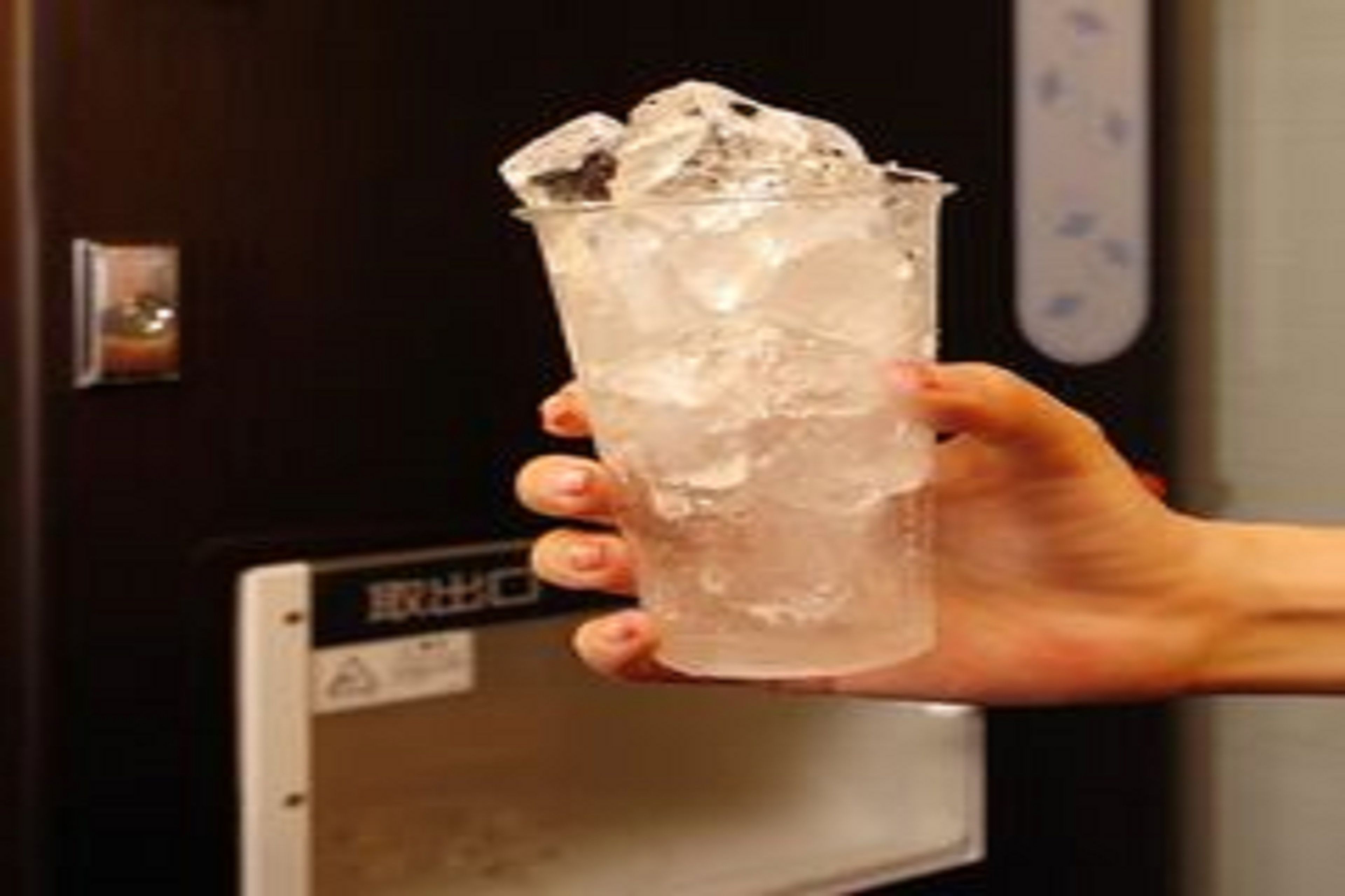 Una mano sostiene un vaso de plástico transparente con cubitos de hielo.