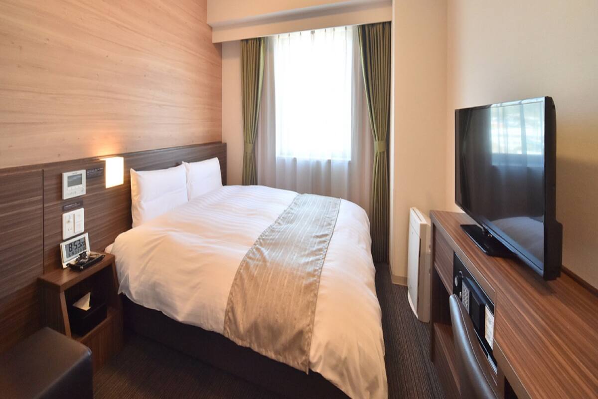 Habitación de hotel con una cama grande, televisor de pantalla plana, mesita de noche y panel de control para los servicios de la habitación.