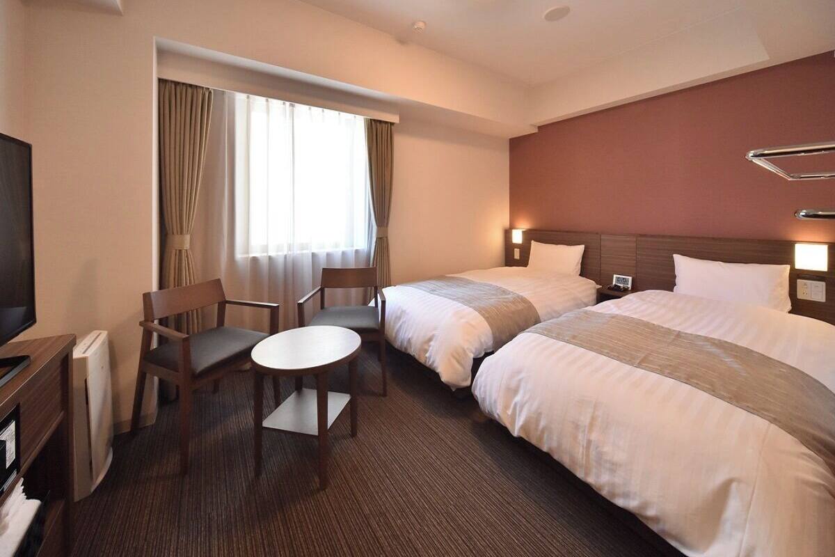 Habitación de hotel con dos camas, un escritorio, una silla y un televisor.