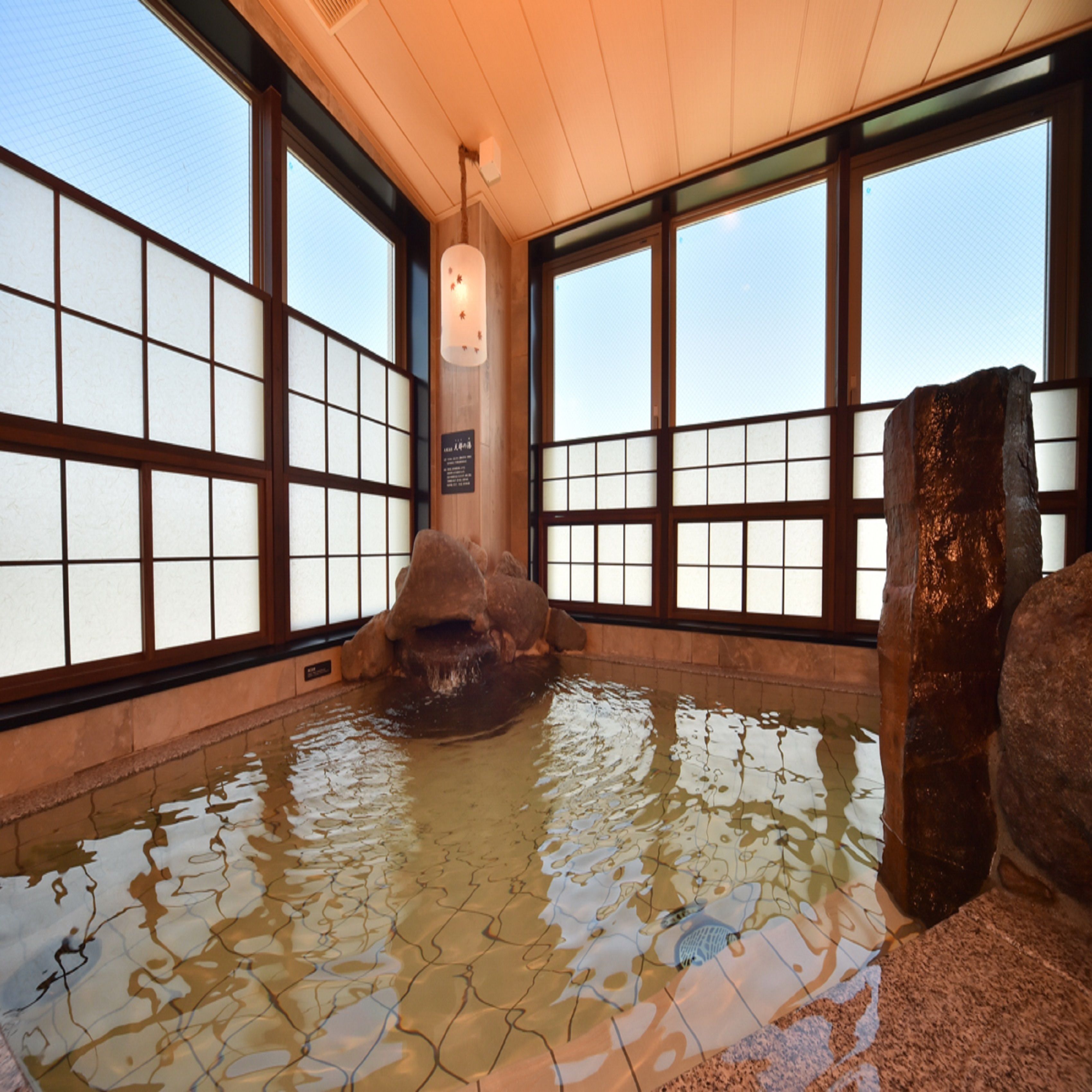 A traditional Japanese onsen with tiled floors, wooden frames, and a rock formation in the center.