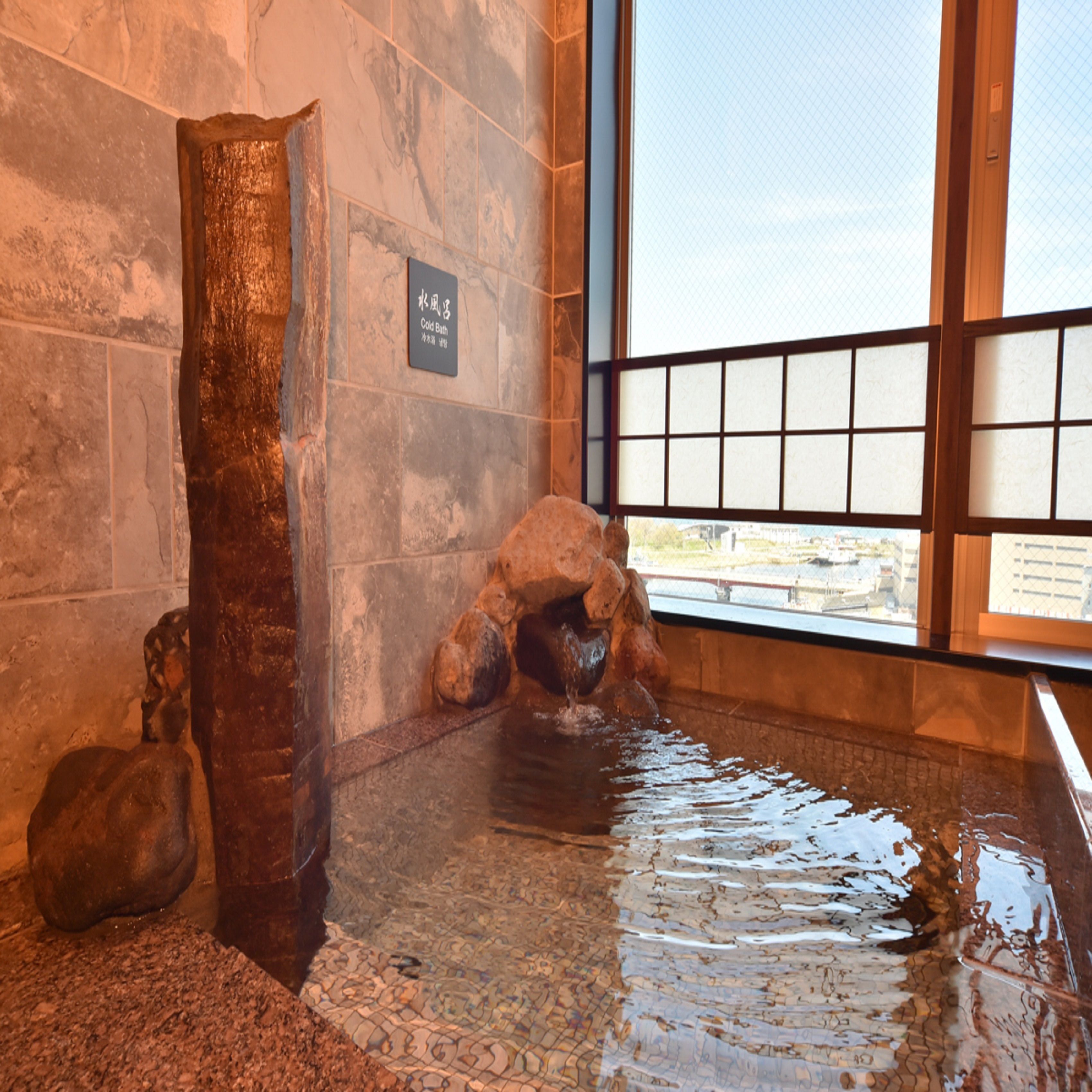 A stone wall with a sign reading "Cold Bath" and a window with a view of buildings.