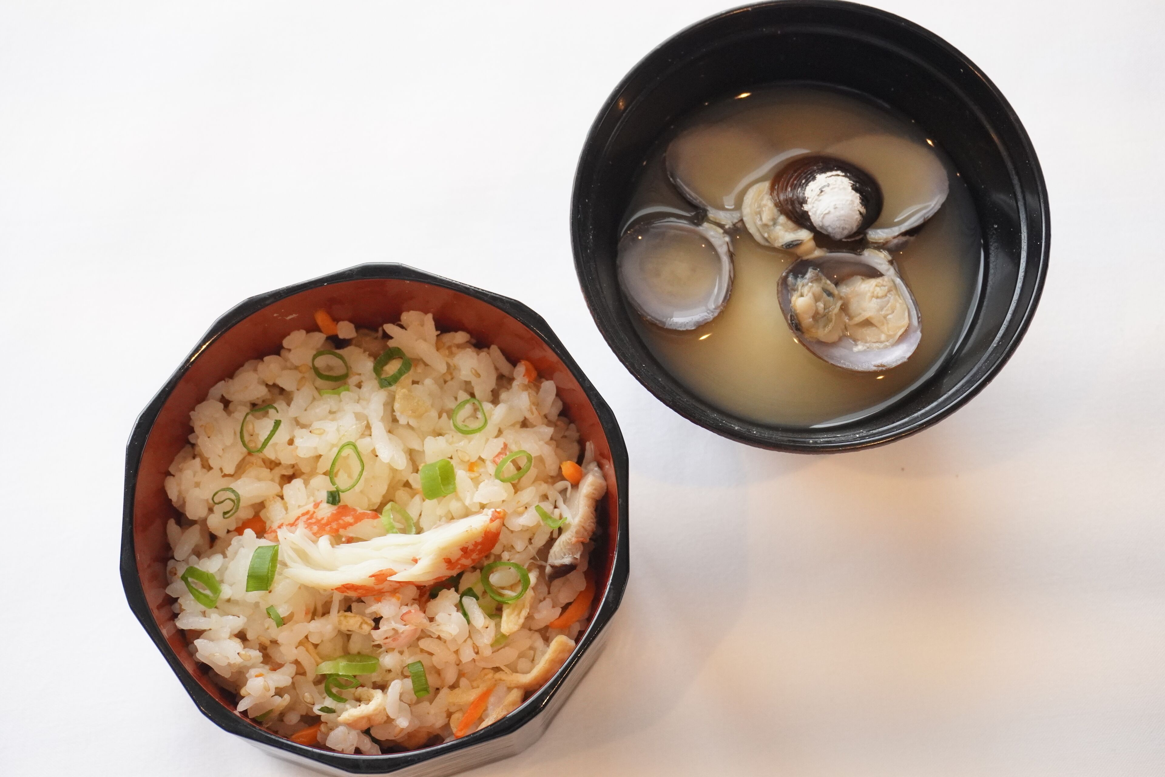 A bowl of rice with vegetables and a bowl of soup with clams.