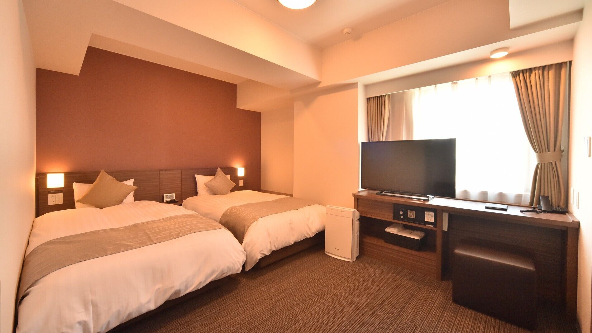 Une chambre d’hôtel avec deux lits, une télévision, un bureau et une fenêtre avec des rideaux.