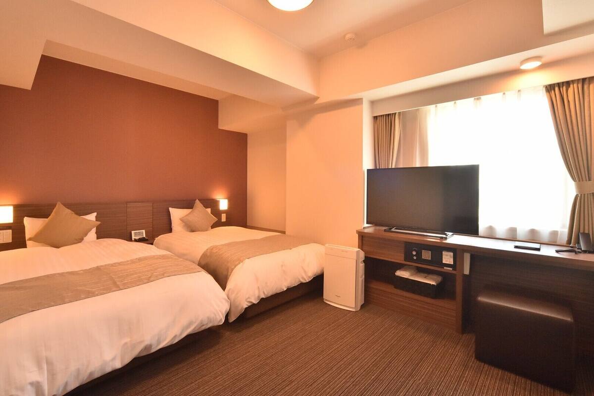 Habitación de hotel con dos camas, televisión, escritorio y ventana con cortinas.