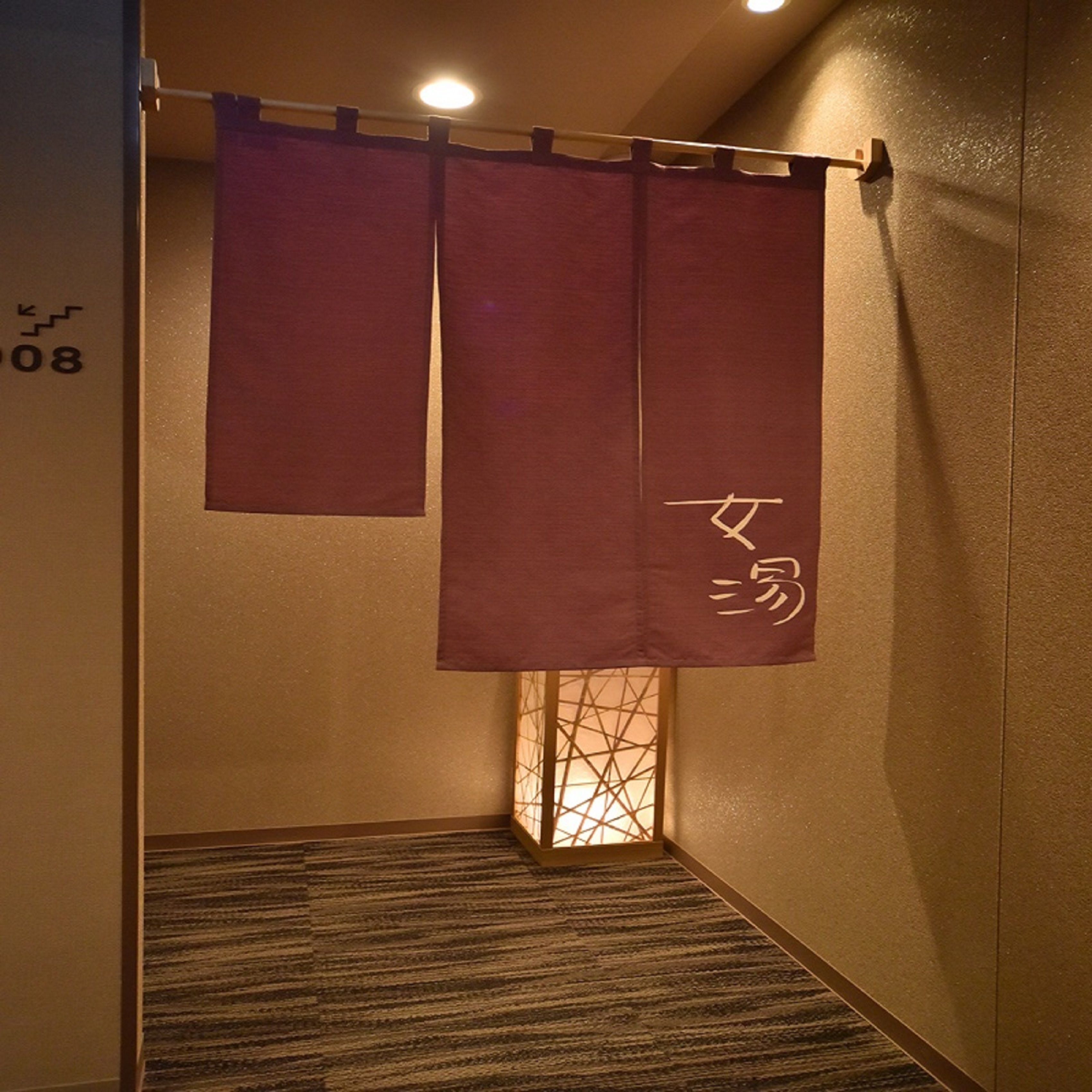 A room with a carpeted floor, a curtain with Japanese characters, and a small window with a geometric pattern.