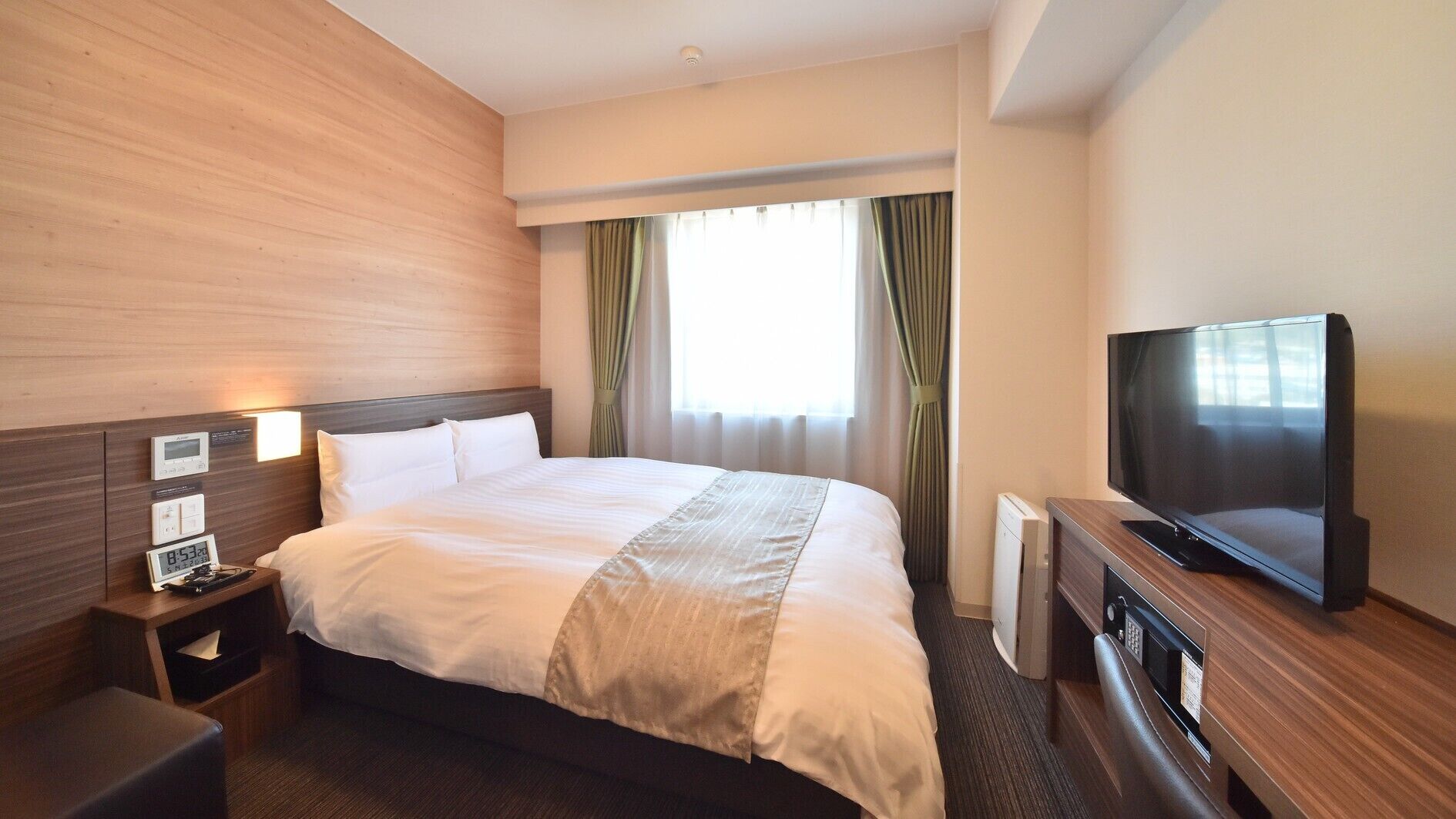 Une chambre d’hôtel avec un lit, des tables de chevet, une télévision et une fenêtre avec des rideaux.