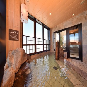 Ett traditionellt japanskt onsen-bad med träinredning, stora fönster och ett stenbassäng för vattnet.