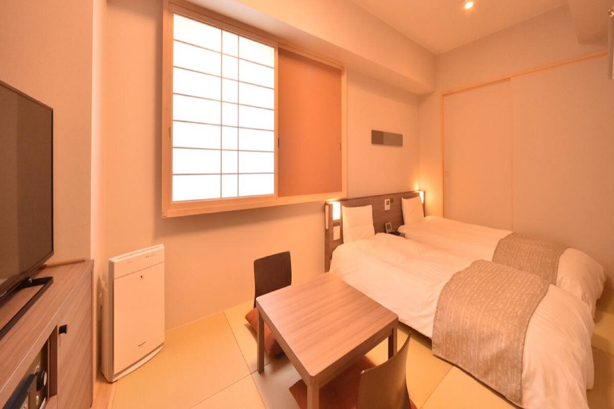 Una habitación de hotel con cama, escritorio, silla, televisión y ventana.
