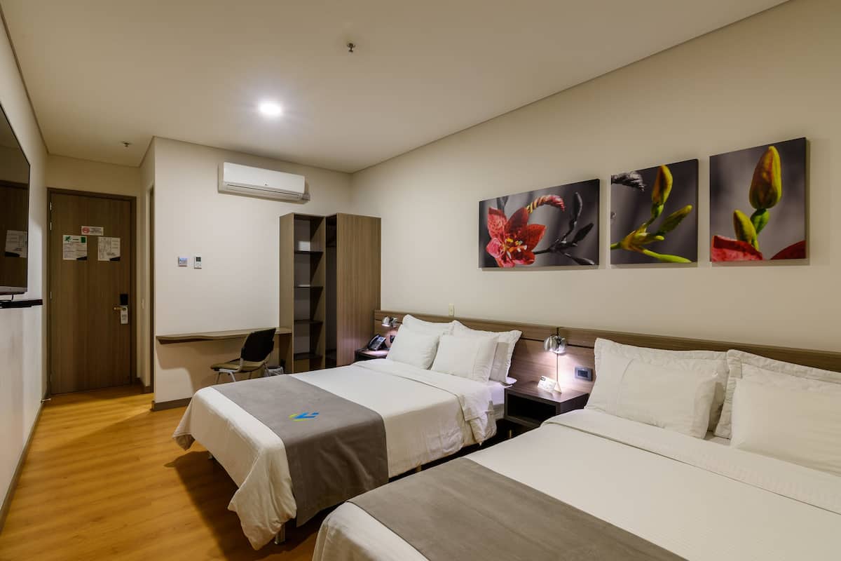A hotel room with two beds, a desk, a chair, and a wall-mounted air conditioner.