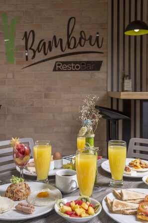 Una mesa de desayuno con diversos platos, como huevos, tostadas y fruta, además de vasos de jugo de naranja.