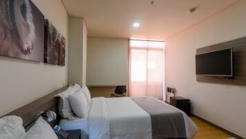 A hotel room with a bed, a desk, a chair, a TV, and artwork on the wall.