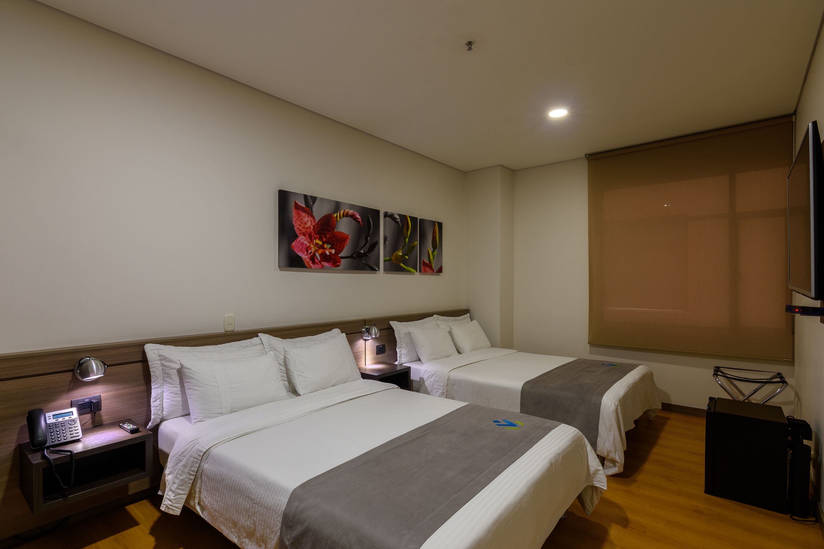 A hotel room with two beds, a bedside table with a lamp, a phone, and a TV on a stand.